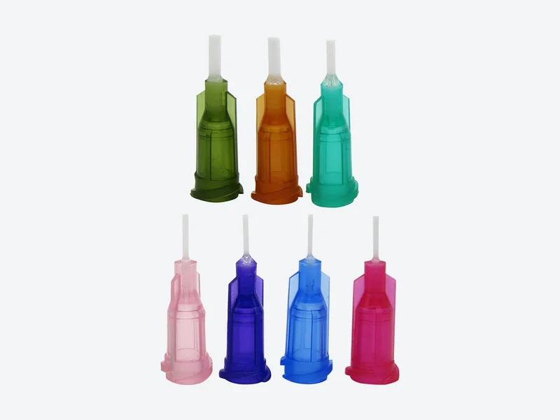 Show a close-up: Seven flexible dispensing needles with short white plastic tubes and color-coded hubs